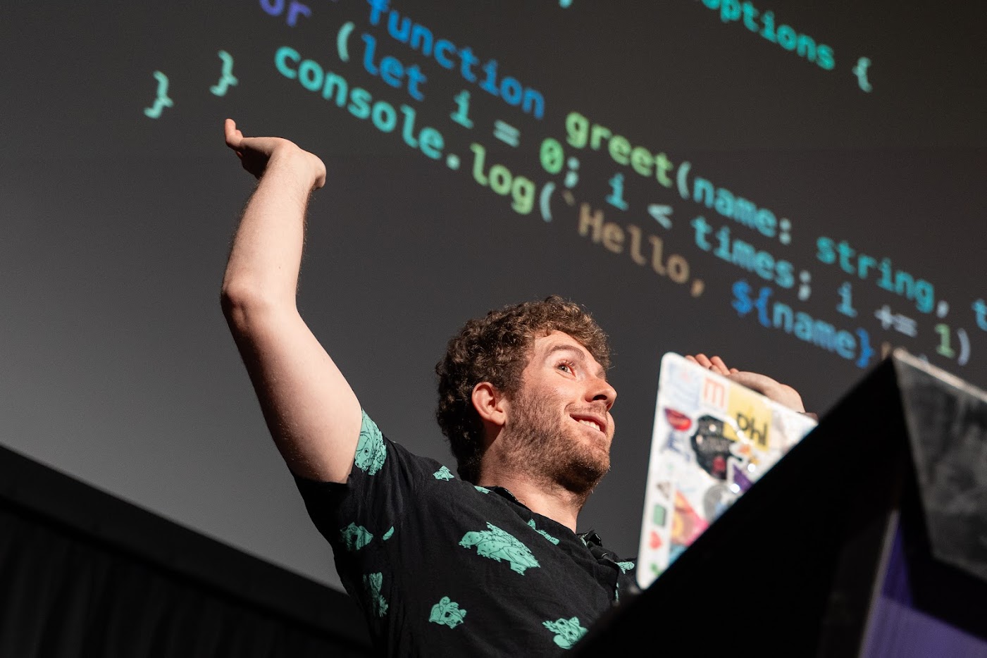 Me raising hands happily while giving a talk on stage, with code projected behind me