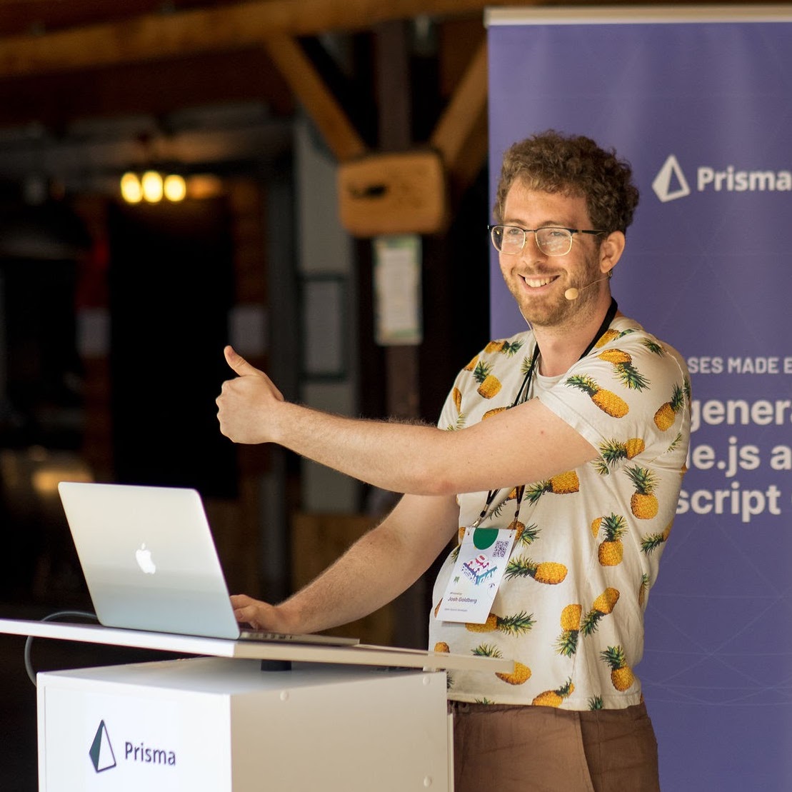 Me smiling and speaking at a conference podium, wearing a pineapples-on-white t-shirt, giving a thumbs up