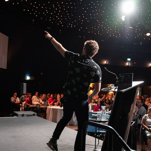 View from behind of me on stage, wearing a black collared shirt with a green Pokemon pattern, pointing to the distance